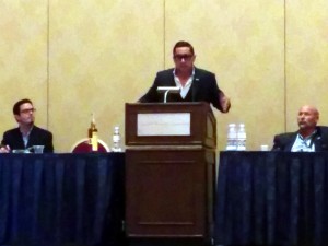 Photo of Lincoln Salazar, CEO/Publisher of Cigar & Spirits magazine, addressing IPCPR 82 attendees from a dias at a cigar and bourbon pairing.